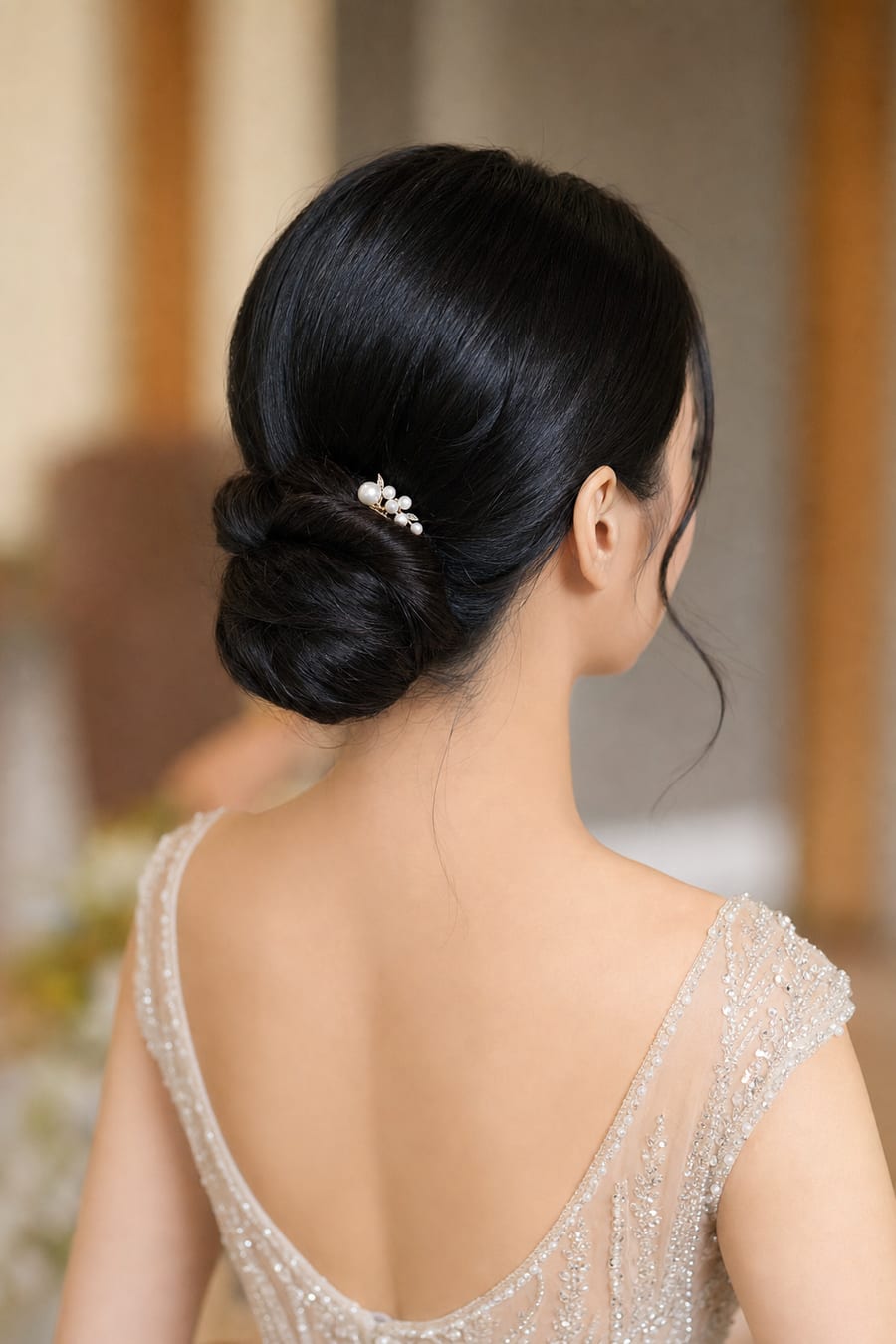 East Asian bride with sleek straight black hair in a low chignon updo held by a pearl pin, back view